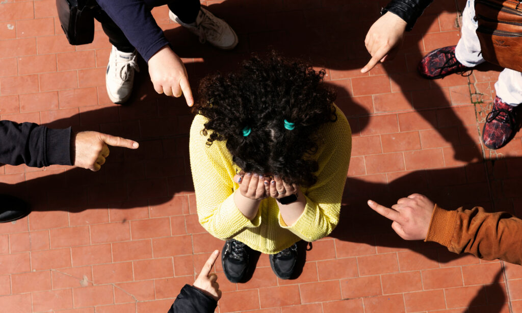 Fotografía desde arriba de una niña en el centro, angustiada, mientras es señalada por un grupo de compañeros que la rodea, fotografía utilizada para la entrevista a Anna Serra, que invita a descubrir qué busca el profesorado en un taller de sensibilización de Bullying, y cómo se vive desde dentro