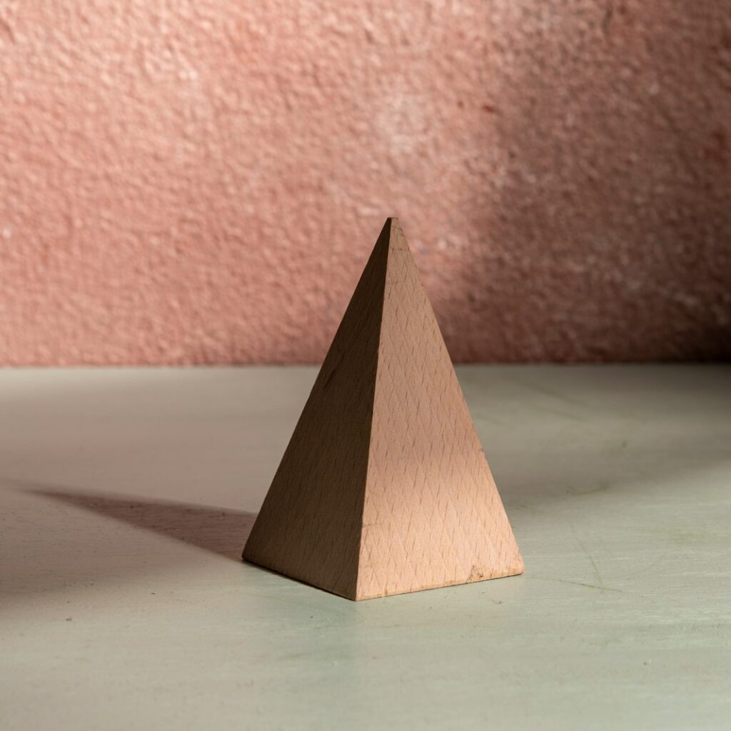 A brown pyramid stands with its strong shadow.