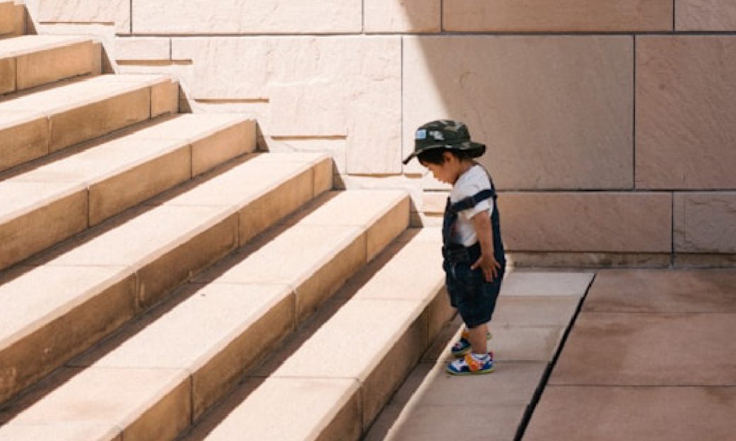 Fotografía de un niño frente a una gran escalera mientras mira fijamente el primer escalón, utilizada para el reto "Normal Challenge", que se trata de efectuar acciones y trabajo en el aula para generar un cambio positivo hacia los demás